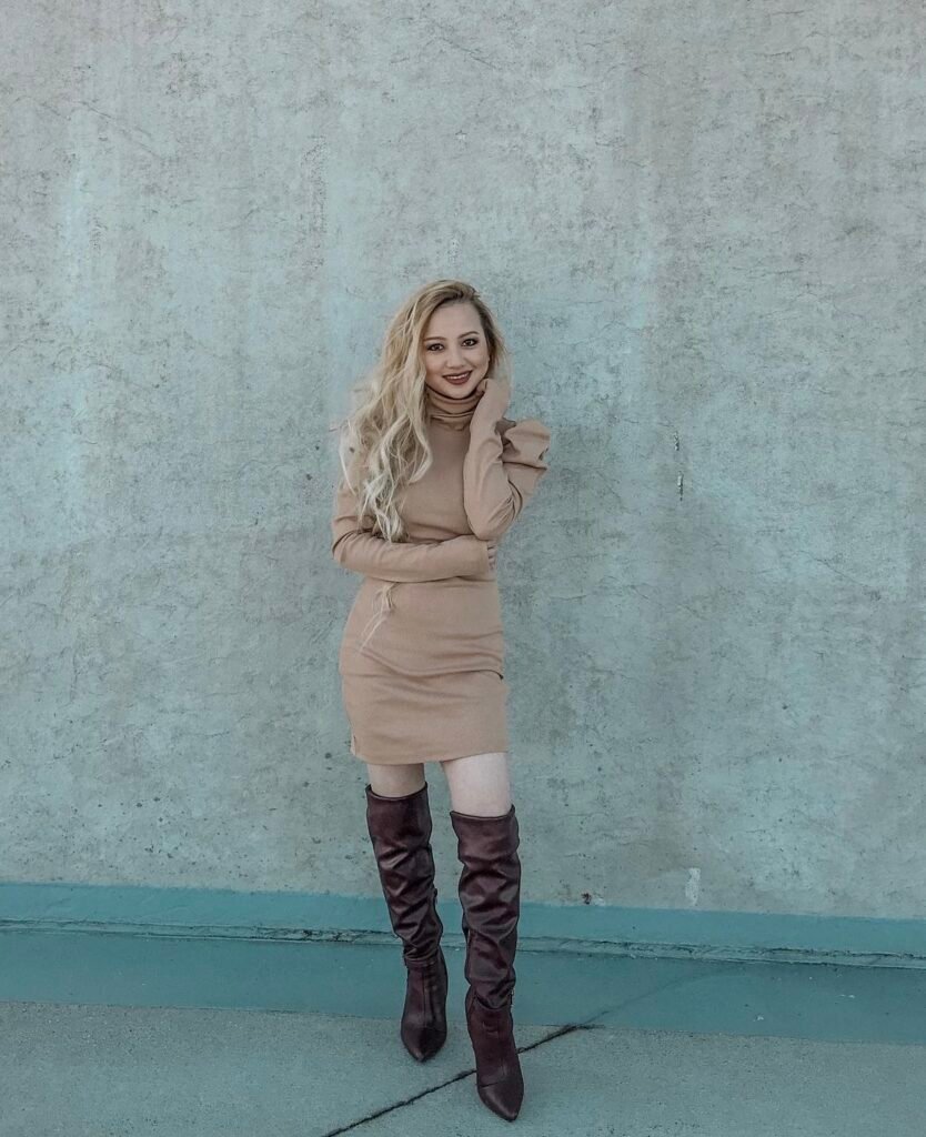 A woman wearing a brown turtleneck dress and brown knee-high boots.