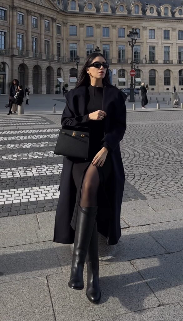 A woman wearing a black long dress with a wool coat and high boots.