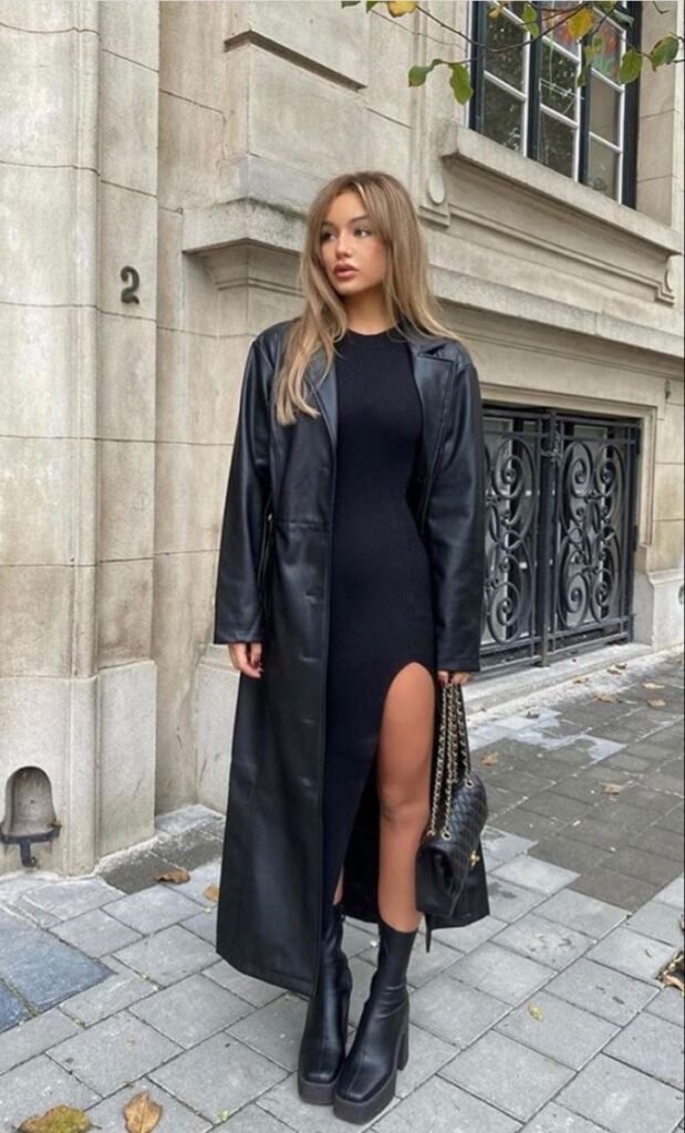 A woman wearing a black long dress with a leather trench coat.