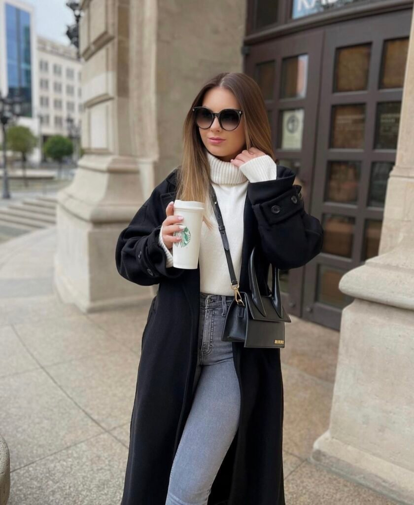 A black wool trench coat with a white sweater and jeans.