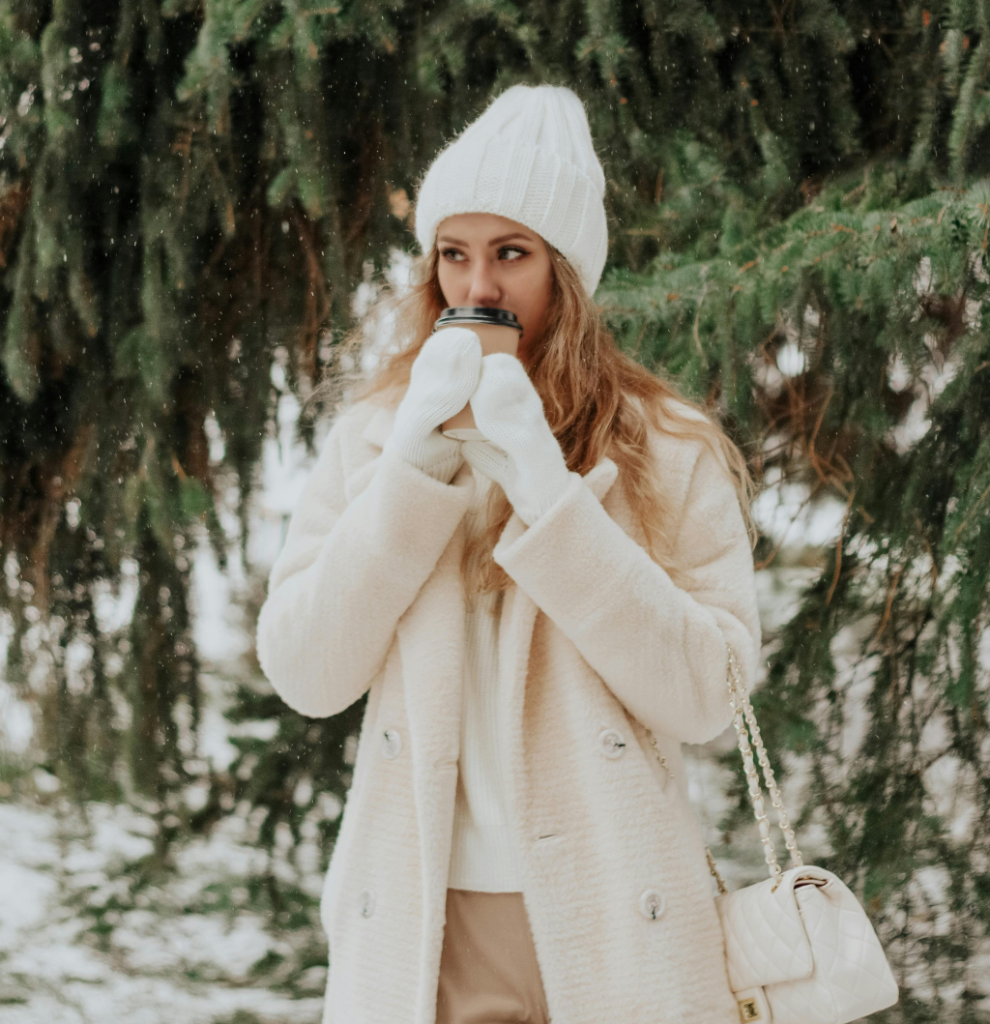 A woman with a white knit cap and gloves, a cream coat, sweater and bag.