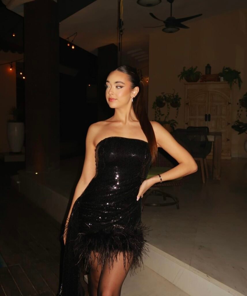 A woman wearing a short black glitter dress with feathers.